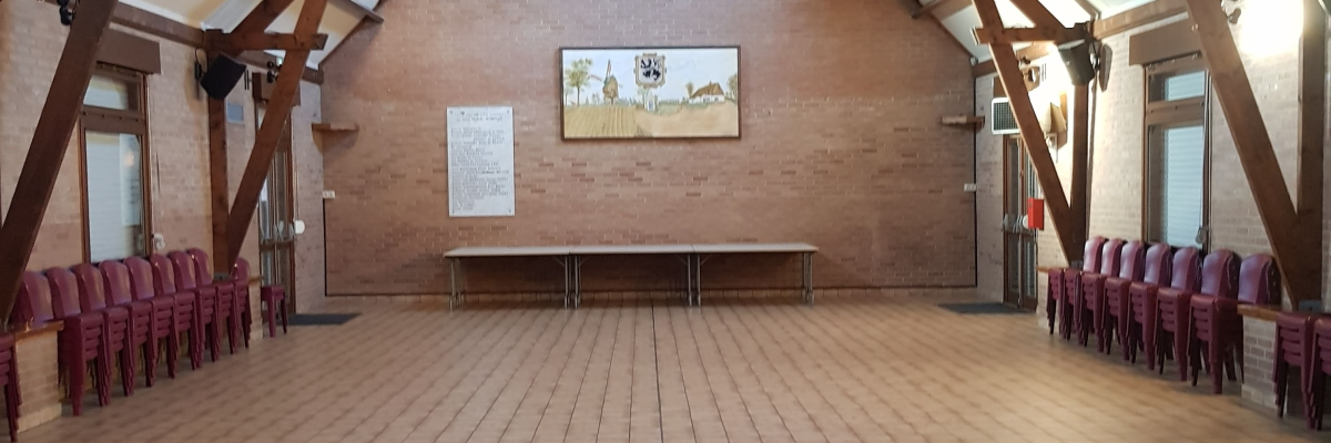 Salle avec poutres apparentes, chaises, table et tableau au mur.