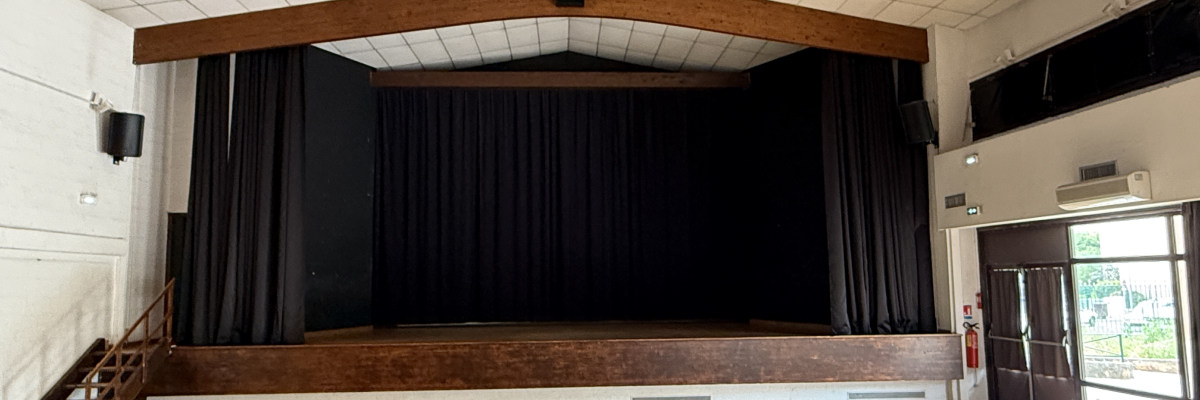 Salle avec scène, bois, rideau, haut-parleurs, projecteur.