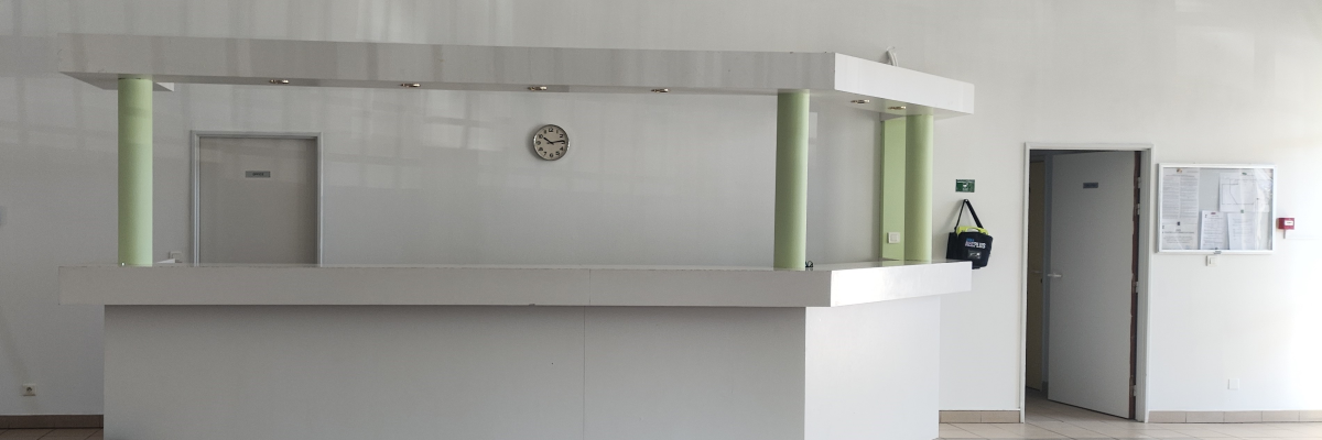 Réception avec comptoir, colonne, horloge, sac, porte, panneau d'affichage et poubelle.