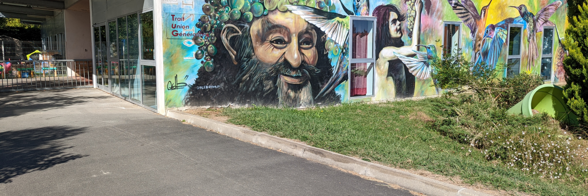 Mur extérieur avec graffiti coloré, entrée vitrée, allée, gazon et arbres.
