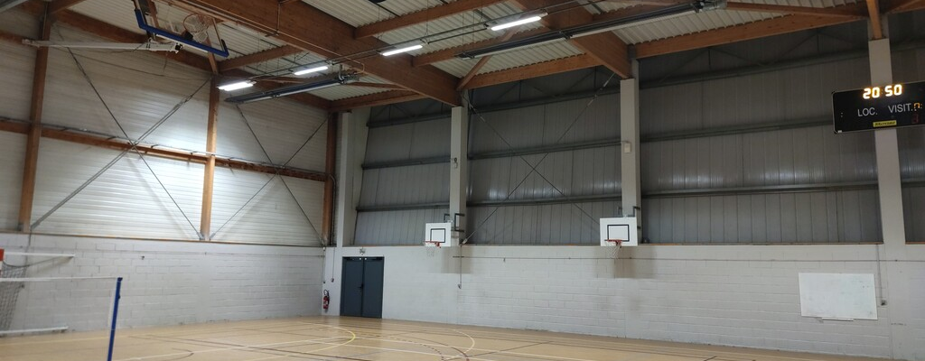 Salle de sport avec paniers de basket, terrain de jeu, panneau d'affichage et projecteurs.