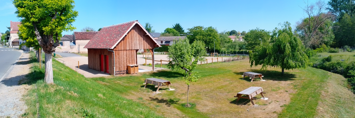 Cabine en bois, tables de pique-nique, arbres, route, maisons.
