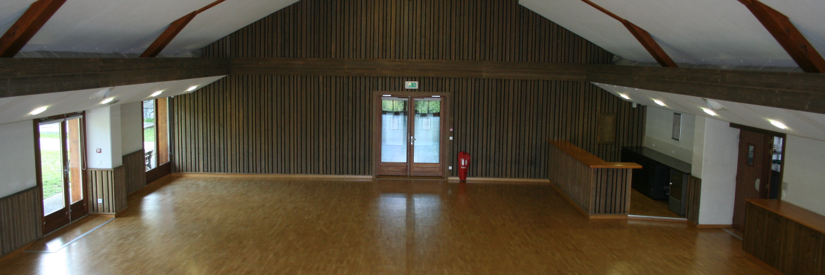 Salle vide avec plancher en bois, poutres apparentes, fenêtres, portes.
