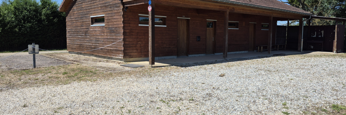 Bâtiment en brique avec toit en tuiles, portes et fenêtres, situé dans une zone gravillonnée.