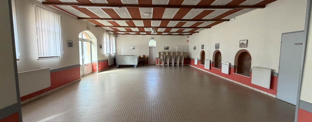 Salle spacieuse avec sol carrelé, murs blancs, plafond en bois, portes et fenêtres.