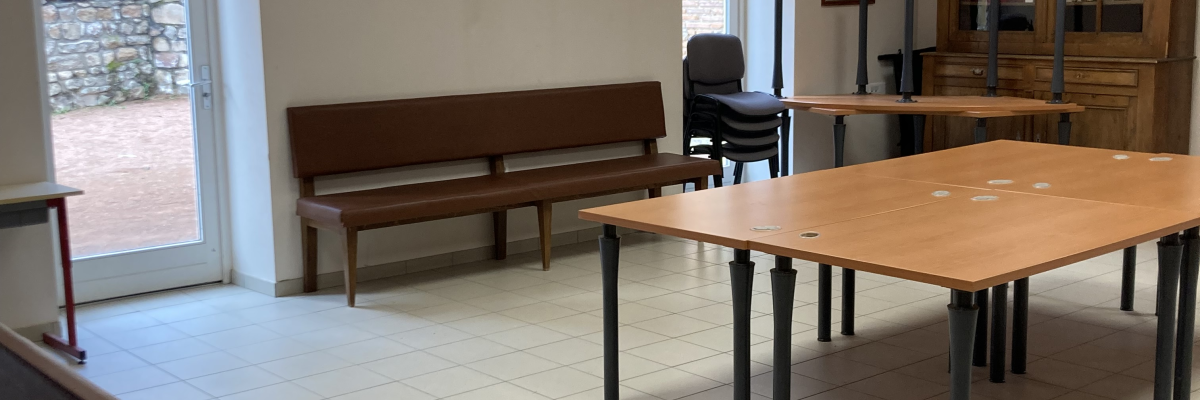 Salle avec tables, chaises, bancs, étagères et luminosité naturelle.