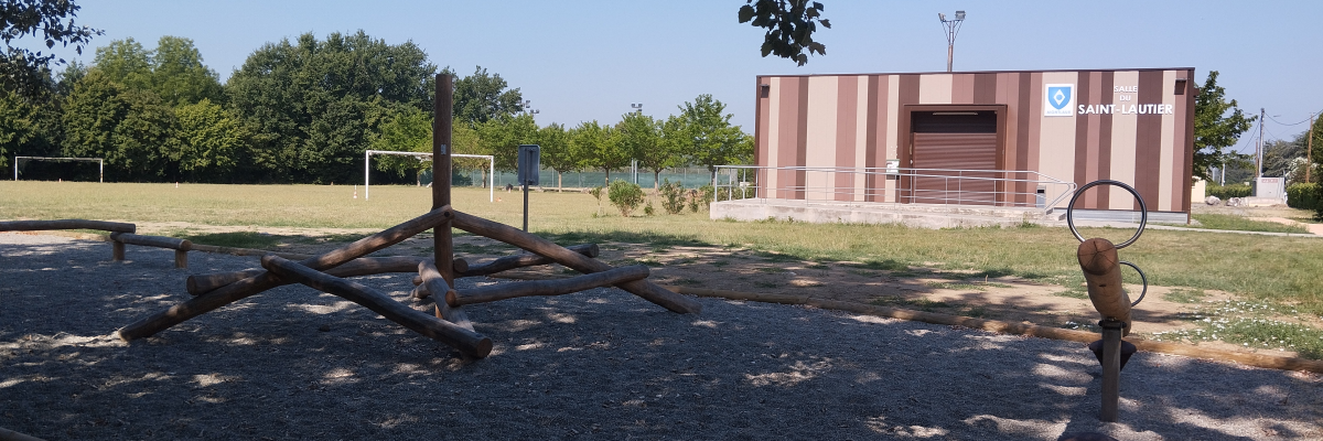 Terrain de sport avec panier de basket, structure en bois et bâtiment en arrière-plan.
