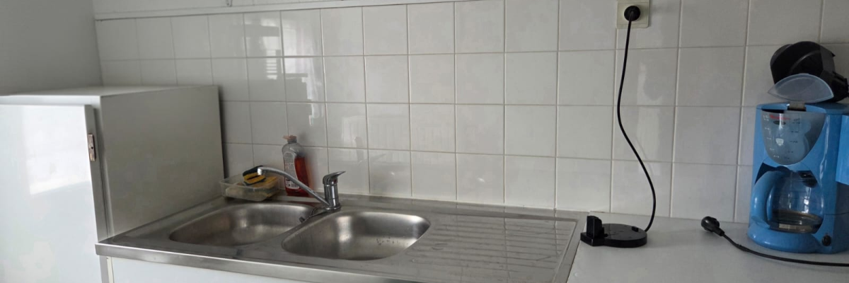 Cuisine avec évier, cafetière, étagère à condiments, et plaques de cuisson.