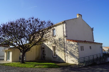 Maison blanche avec portail, arbre et toit rouge.