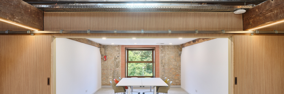 Salle avec.table, chaises, chariot de nettoyage, portes en bois et fenêtres.