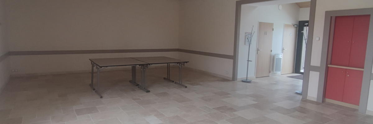 Pièce avec table, chaises, projecteur, porte rouge et sol carrelé.