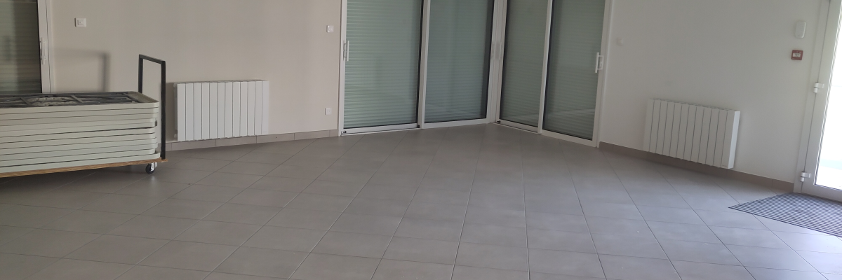 Salle vide avec portes vitrées, radiateurs et sol carrelé.