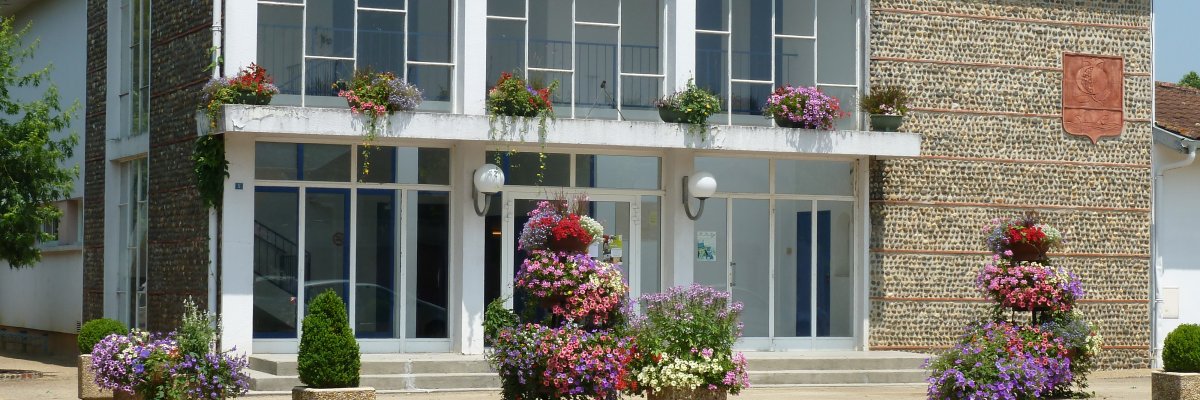 Bâtiment avec façade en brique, grandes fenêtres, fleurs en pots et entrée centrale.