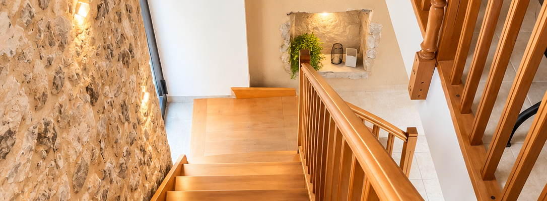Escalier en bois avec rampe, mur en pierre, sortie de secours, éclairage mural.