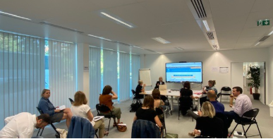 Salle de réunion avec table, chaises, écran, ordinateur, projecteur et personnes assises.