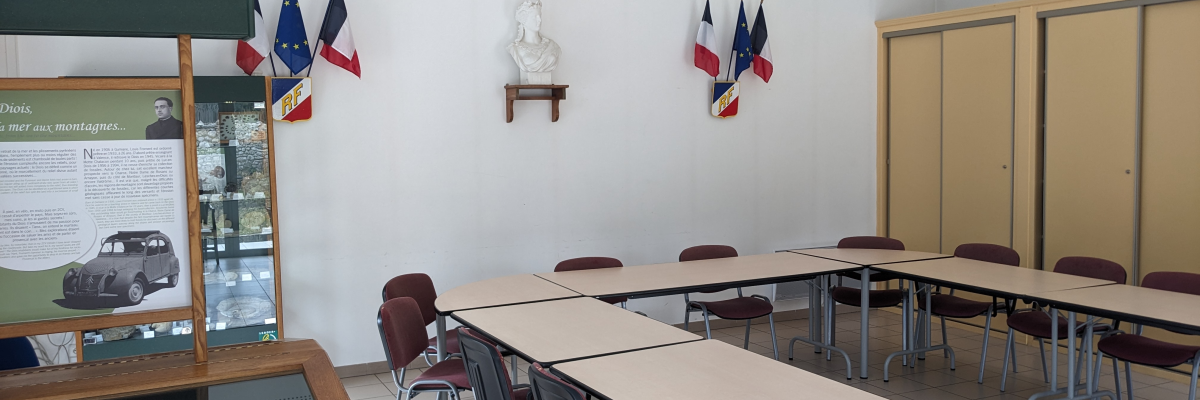 Salle de classe avec tables, chaises, tableau et affichages muraux.