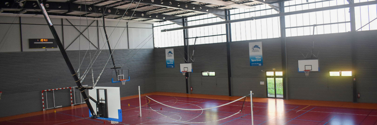 Salle de sport avec filets, paniers de basket, et gradins.