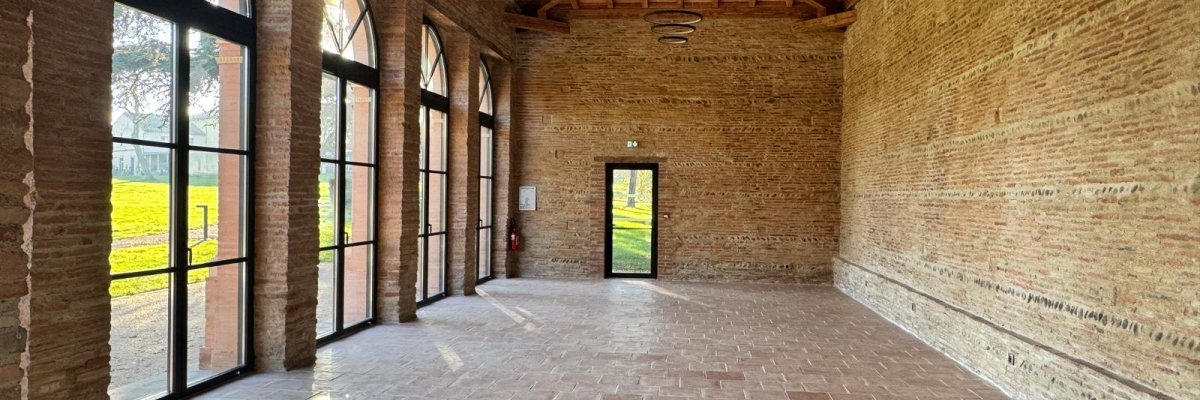 Pièce vide avec murs en brique, sol carrelé, grandes fenêtres et lumière naturelle.