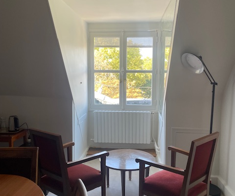 Pièce avec deux chaises, table ronde, radiateur, fenêtre, porte et lampe sur pied.