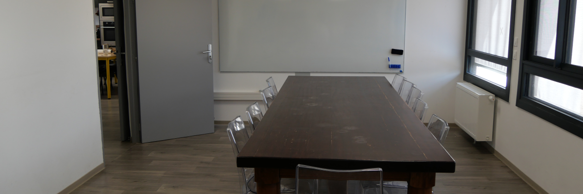 Salle avec table, chaises, tableau blanc, vidéo projecteur et radiateur.