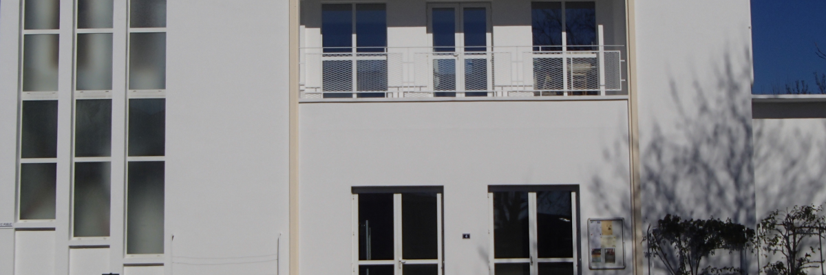 Bâtiment blanc avec grandes fenêtres, porte et panneau d'affichage.