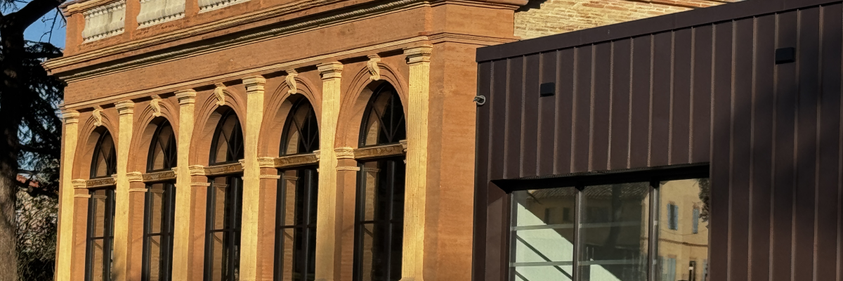 Bâtiment avec structure en brique et grandes fenêtres, extension moderne avec porte en verre.