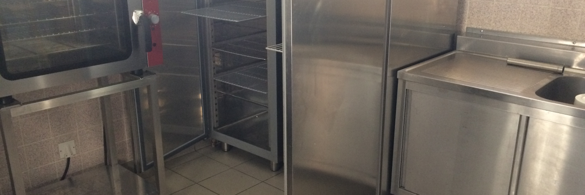 Cuisinière, étagères, réfrigérateur, et lavabo en acier inoxydable dans une cuisine.