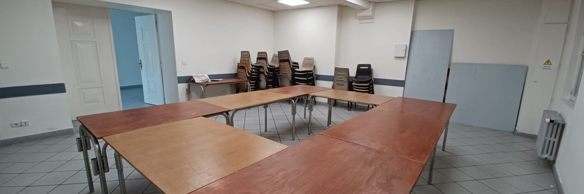Salle avec tables, chaises, porte, radiateur et éclairage.
