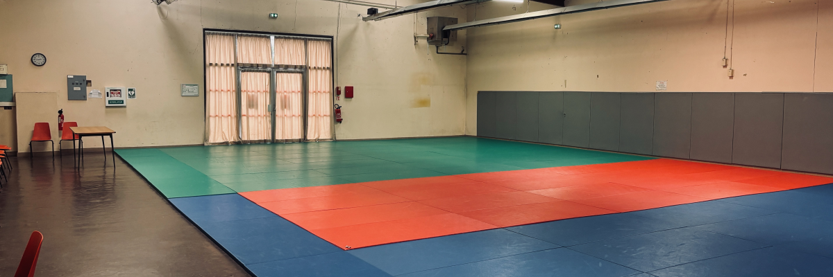 Salle avec tapis de sol coloré, chaises, table, horloge et extincteur.