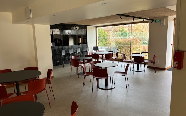 Salle avec tables rondes, chaises, comptoir et distributeur automatique.