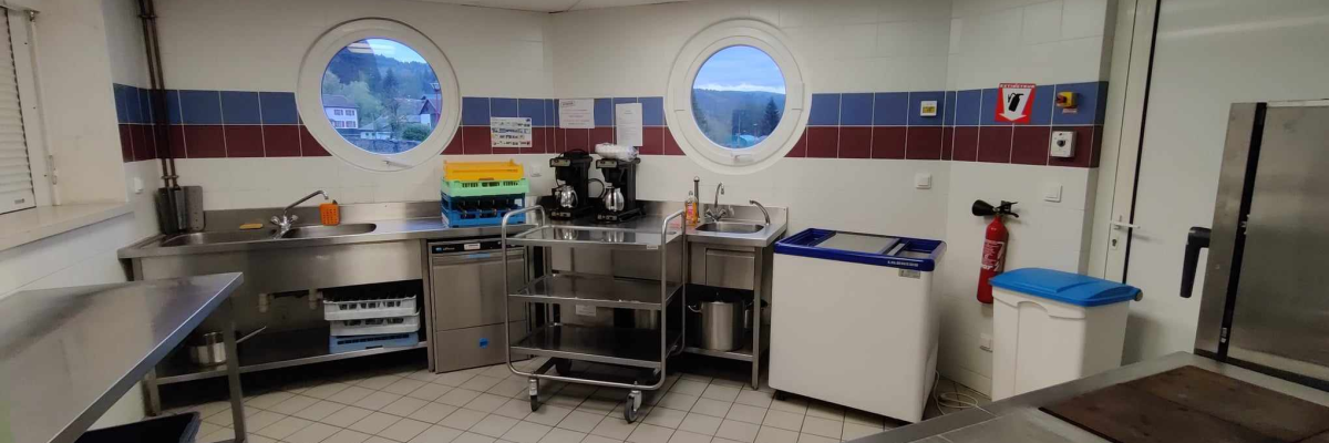 Cuisine avec plans de travail, évier, lave-vaisselle, chariot, frigo, cafetière, fenêtres rondes.