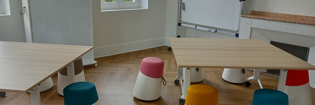 Salle avec tables, tabourets, tableau blanc et étagère.