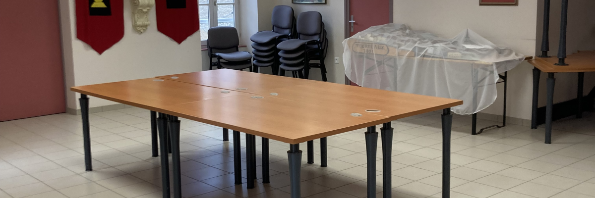 Salle avec table, chaises, bannières, tableau, porte et sol carrelé.