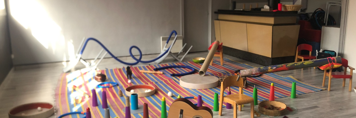 Pièce avec tapis, guitare, instruments de musique, objets divers éparpillés et meuble avec accessoires de cuisine.