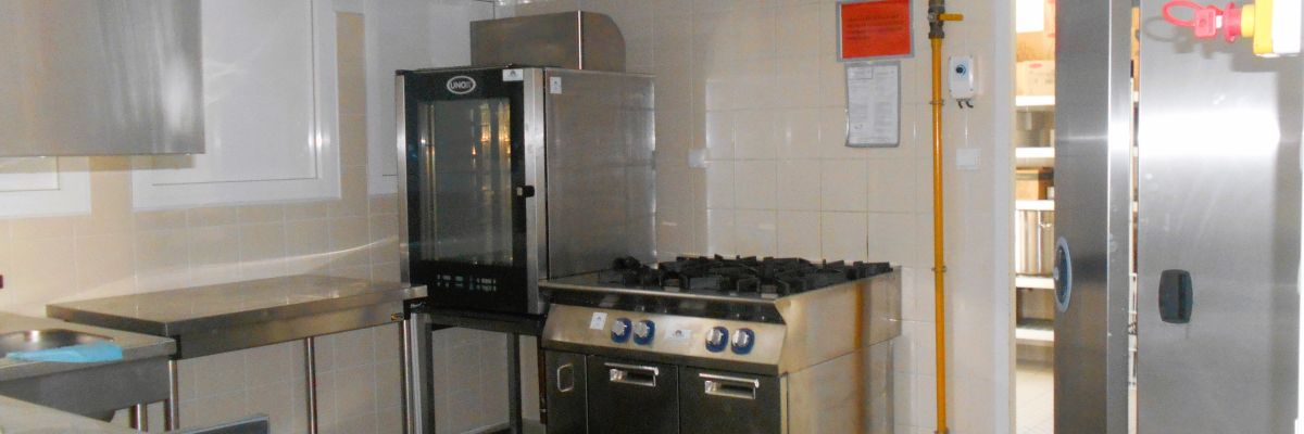 Cuisine professionnelle avec four, plaque de cuisson, réfrigérateur, plan de travail, évier et hotte.