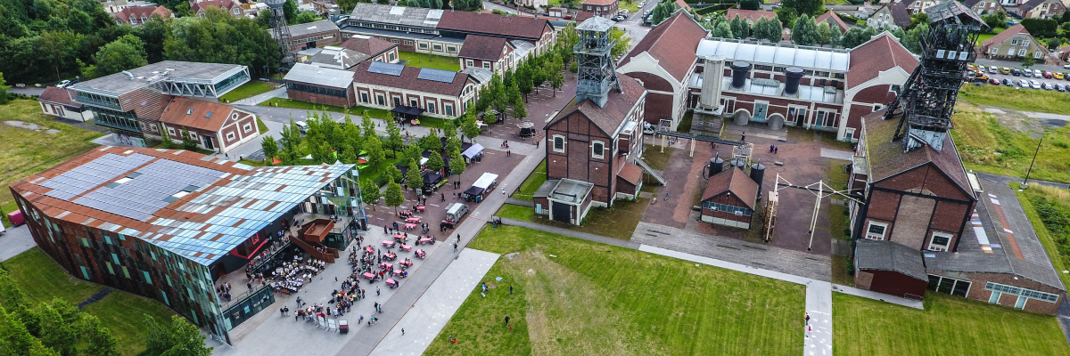 Vue aérienne d'un site industriel avec bâtiments, cheminées, et espace vert.