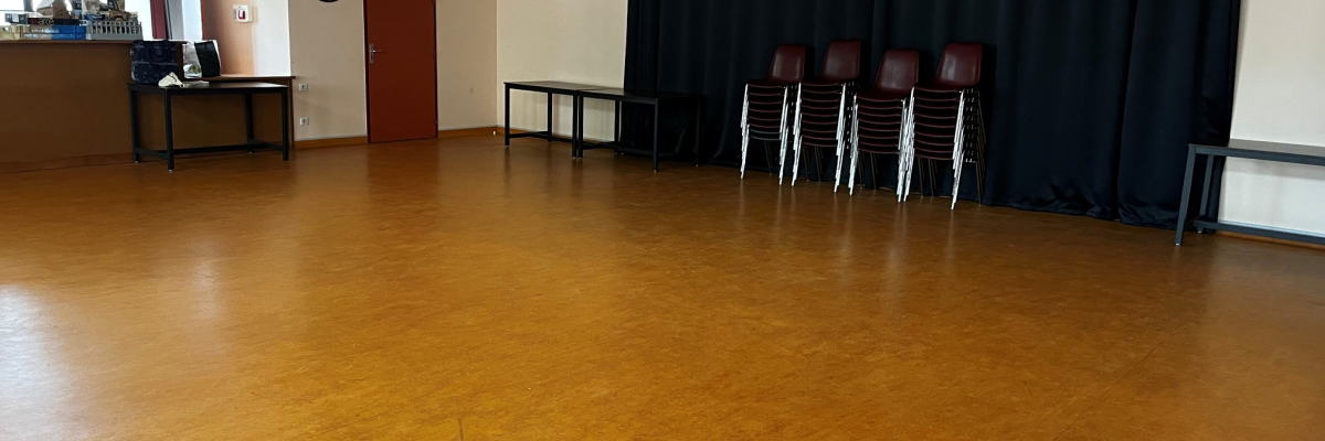 Salle avec parquet, chaises, table, rideau noir, horloge, bureau et porte rouge.