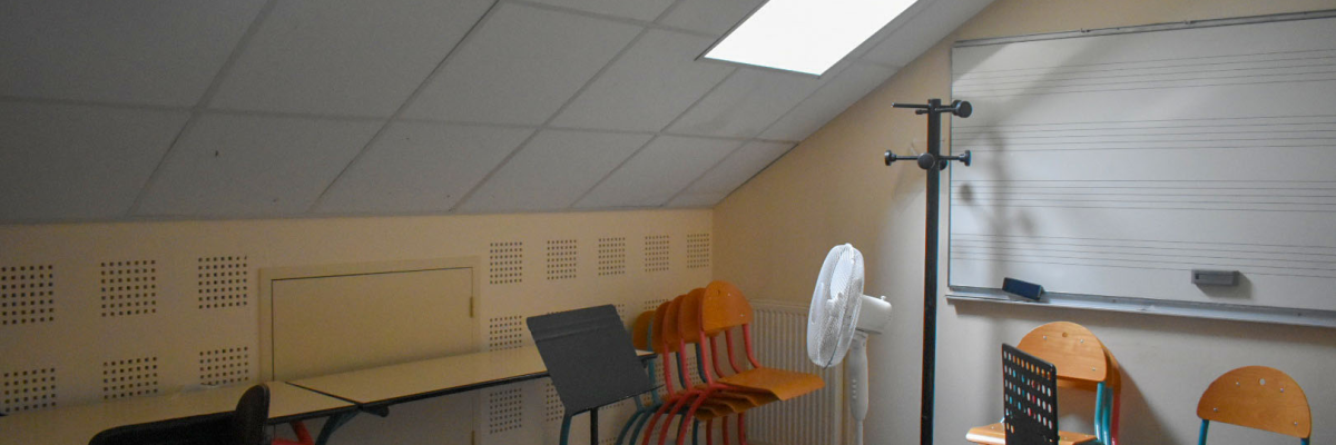 Salle avec tables, chaises, radiateur, ventilateur, porte-manteau et lumières.