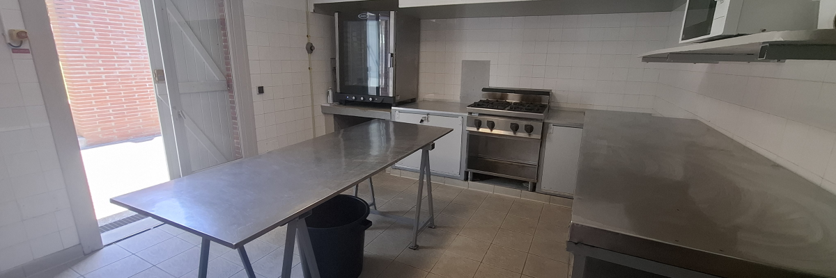 Cuisine avec table, poubelle, plaques de cuisson, évier, micro-ondes et étagères.