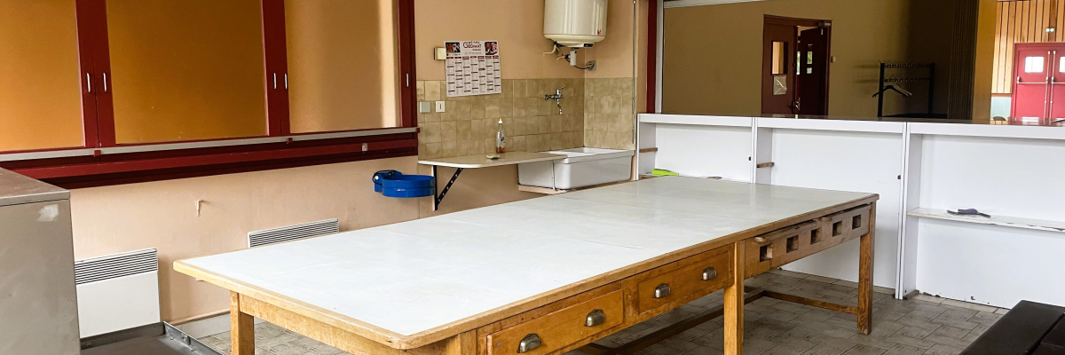 Laboratoire avec table centrale, placards, évier, miroir, chauffe-eau et étagère.