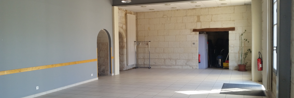 Salle vide avec porte, mur en pierre, porte-manteau, extincteurs et seuil de porte.