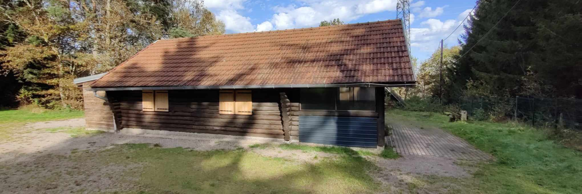 Bâtiment en bois avec toiture en tuiles, porte en métal et arbre derrière.