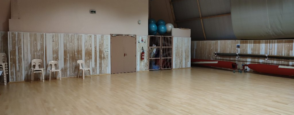 Salle de sport avec tapis de sol, chaises, rameurs, ballons d'exercice et porte.