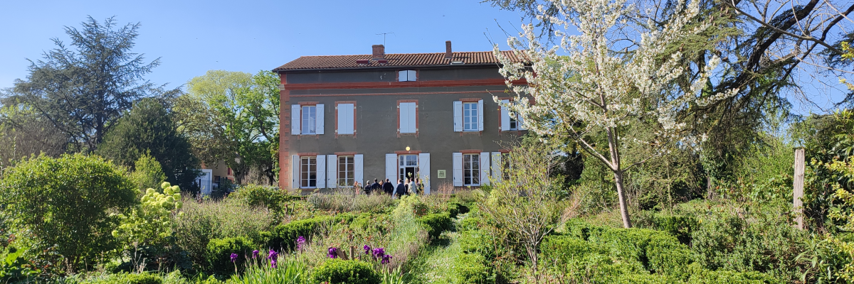 Maison à deux étages avec jardin fleuri et arbres.