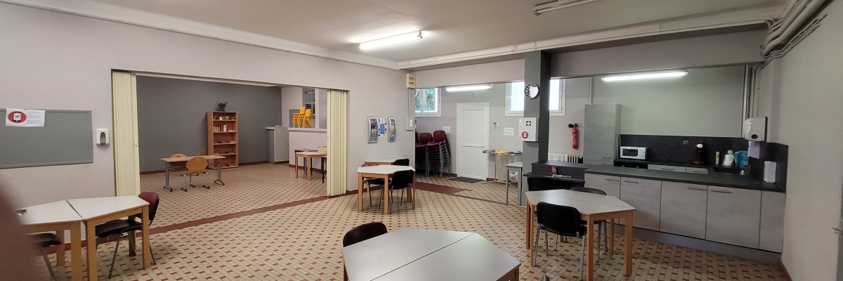 "Salle avec tables, chaises, étagères, micro-ondes, frigo, tableau blanc et extincteur."
