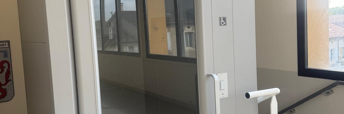 Ascenseur avec porte vitrée, main courante et sol grillagé.