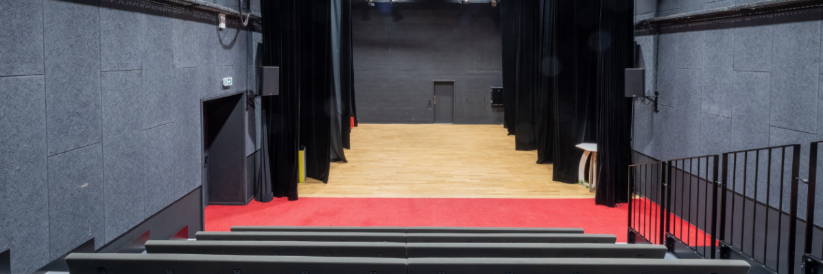 Salle avec gradins, scène, projecteurs et rideaux.