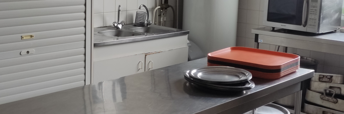 Cuisine avec table, plaques de cuisson, casseroles, réfrigérateur, micro-ondes et étagères.