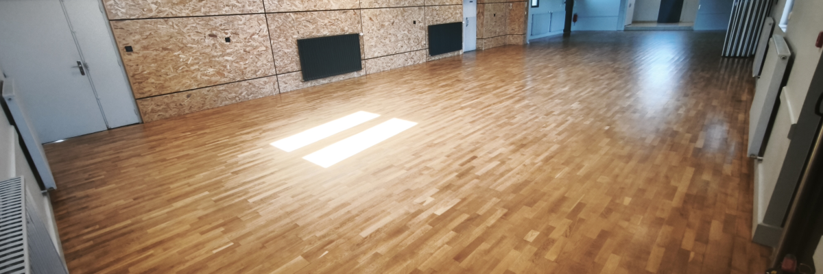 Salle vide avec parois en bois, sol en parquet, portes, extincteur et climatiseur.
