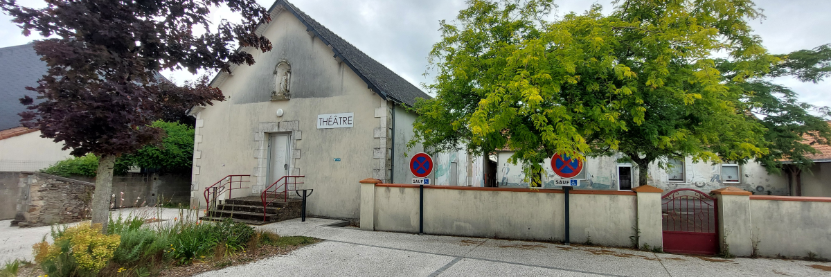 Bâtiment de théâtre avec entrée, escaliers, et panneaux de stationnement interdit.